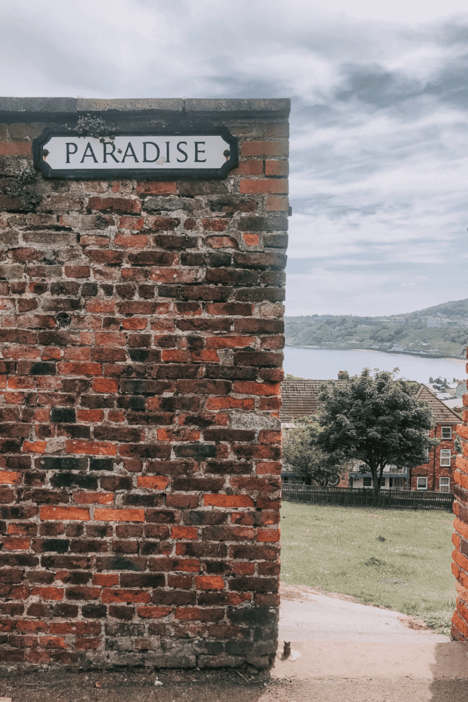 A view to Scarborough bay between a wall with a street sign saying Paradise