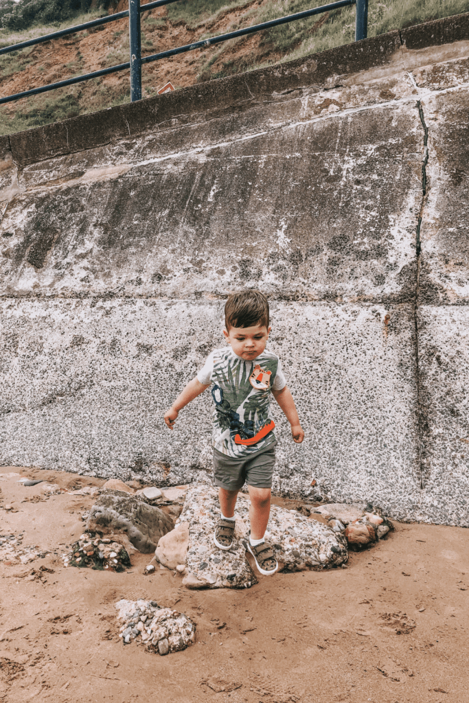 Little boy on beach jumping off a rock in Filey